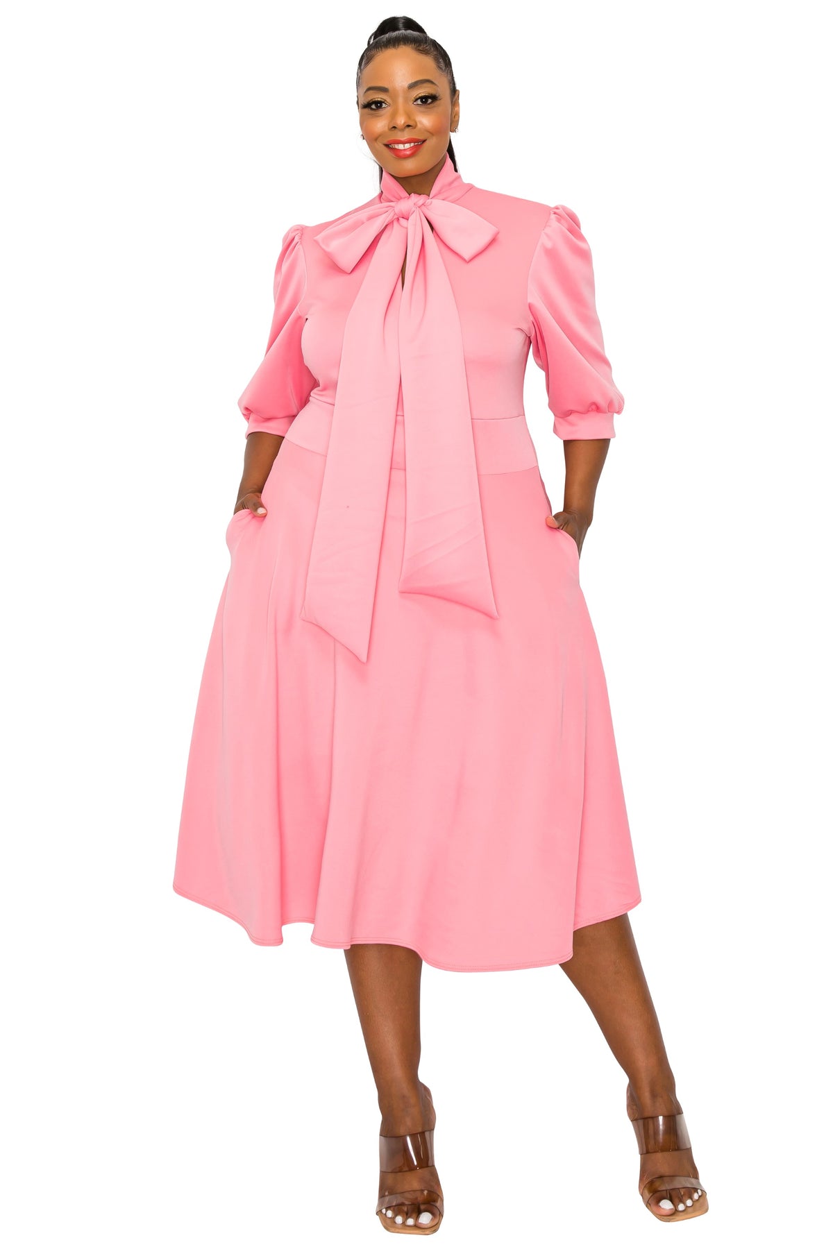 pink plus size flair dress. midi length,  hands in pockets. front view