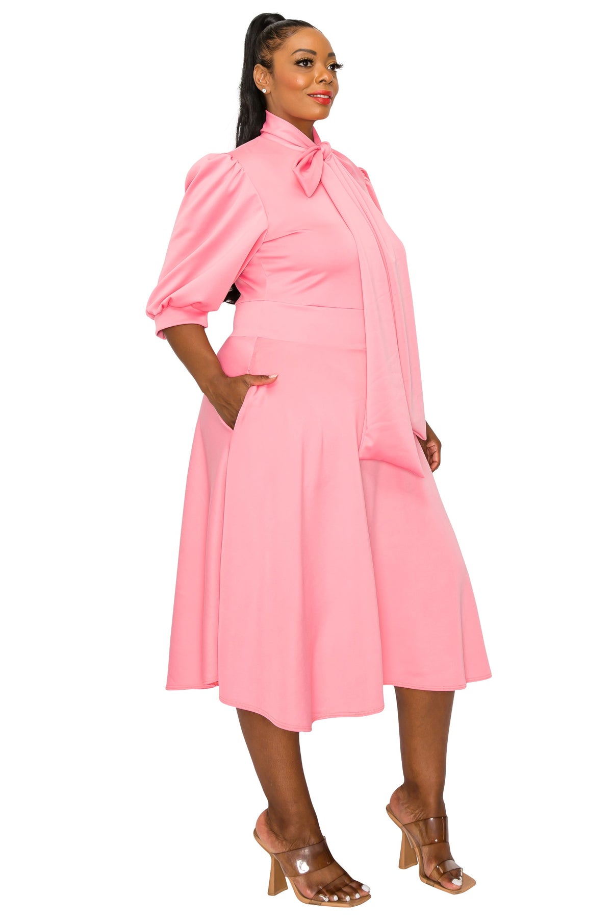 pink plus size flair dress. midi length,  hands in pockets. side view