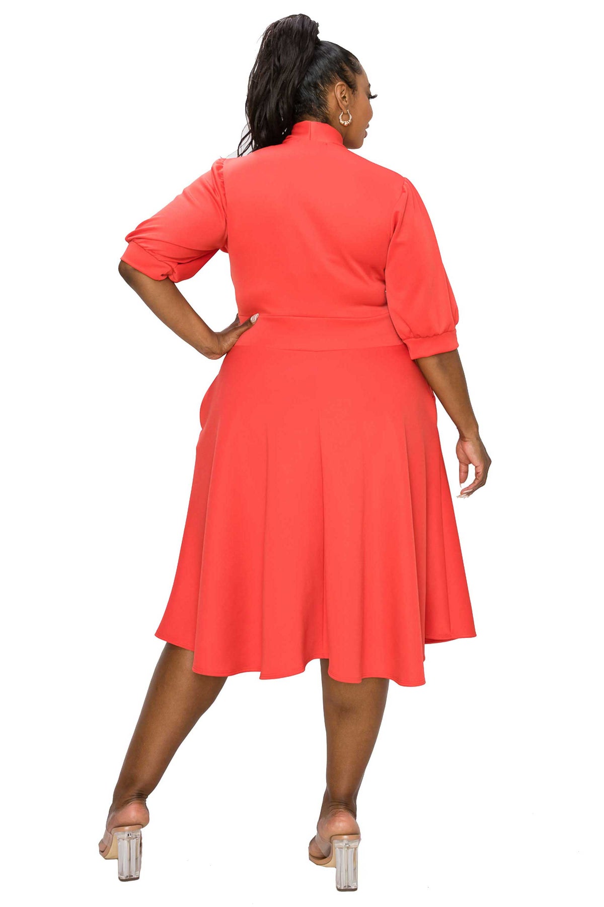 coral red plus size flair dress. midi length,  hands in pockets. back view