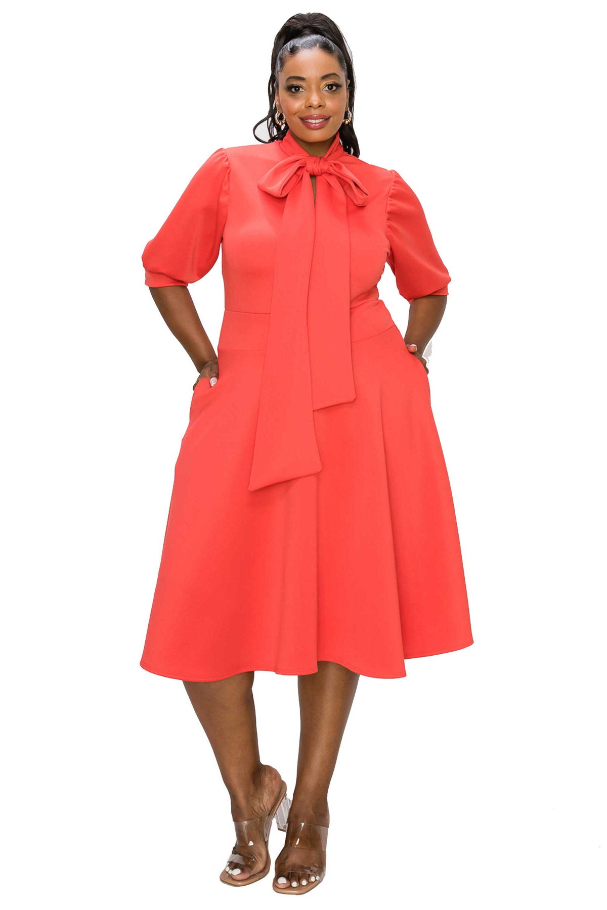 coral red plus size flair dress. midi length,  hands in pockets. front view