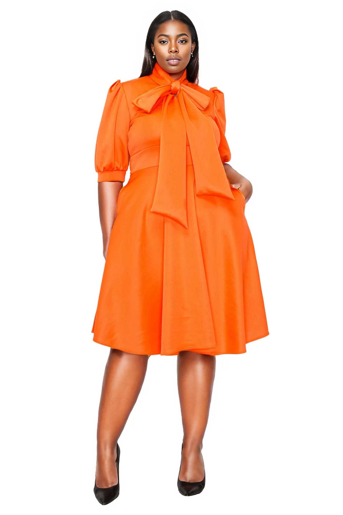 orange plus size flair dress. midi length,  hands in pockets. front view