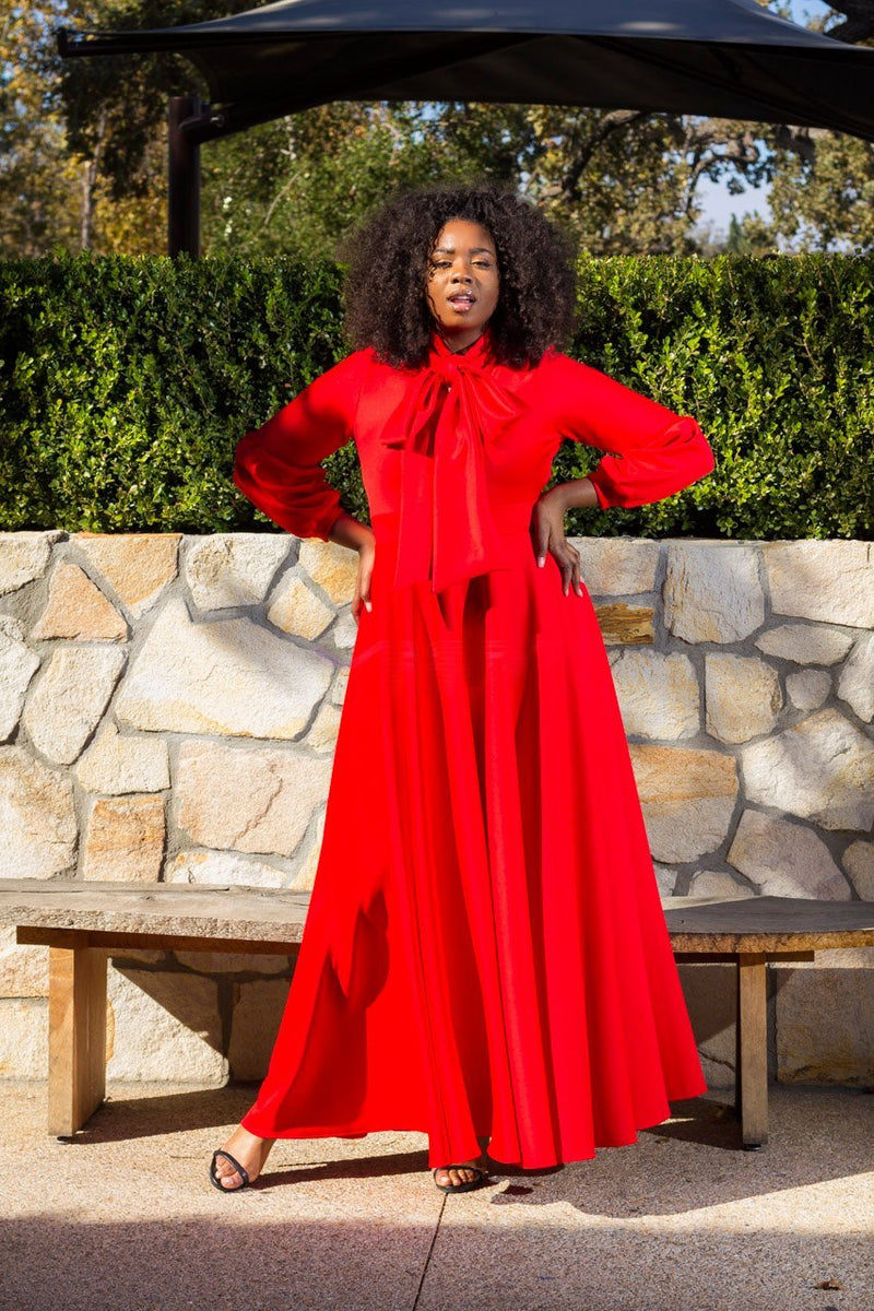 plus size red maxi dress, action lifestyle shot with stone wall and bench and green shrubbery. front view